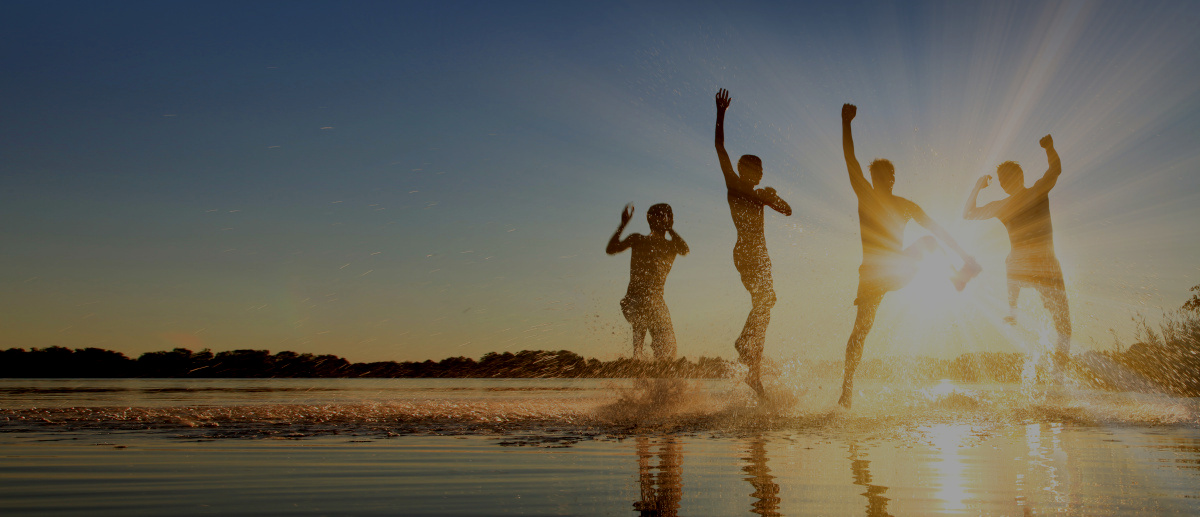 Menschen spielen mit Freude im flachen Wasser im Sonnenuntergang